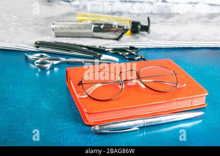 Hairdressing tools set, Red notepad with glasses and scissors, hair clipper, comb, dangerous razor, hair gel stand on blue background Stock Photo