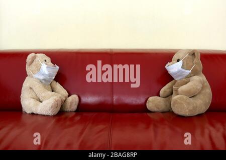 Two teddy bears wearing face masks practicing social distancing on a red couch in the Corona era Stock Photo