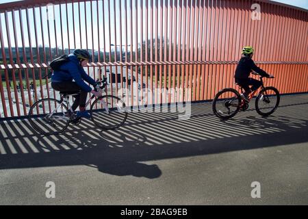 Hackney,London March 2020 during the Covid-19 (Coronavirus) pandemic. Couple cycling on a bridge, Queen Elizabeth Park. Stock Photo