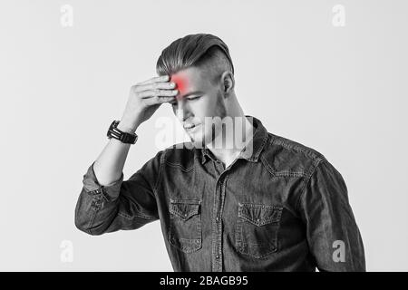 Conceptual image of young man touching his head with hand while isolated on white background. Bearded hipster feeling headache, indicated with red zon Stock Photo