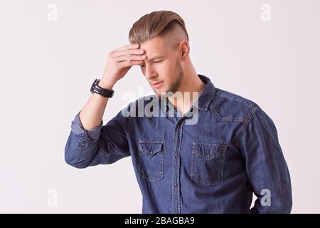 Studio shot of frustrated hipster man touching his head with hand while isolated on white background. Young handsome man feeling exhausted or stressed Stock Photo