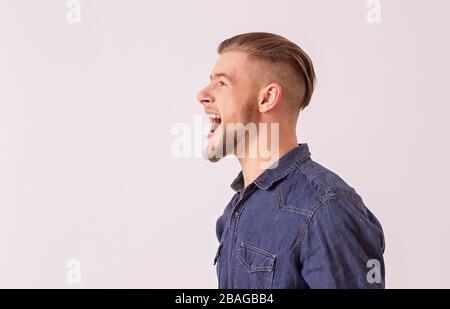 Side view happy, stylish hipster man screaming loudly while isolated on white background with copyspace. Happy bearded man shouting and smiling agains Stock Photo