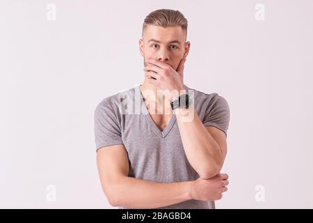 Portrait of surprised young man making face and covering mouth with hand while isolated on white background. Shocked bearded hipster looking to camera Stock Photo