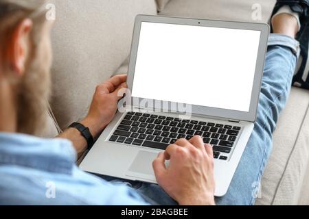 Young male tech user relaxing on sofa using laptop mock up blank white screen. Stock Photo