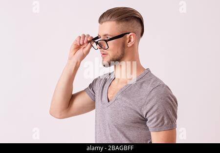 Side view of young business expert wearing eyeglasses and looking away while isolated on white background. Bearded hipster man in t-shirt evaluating o Stock Photo