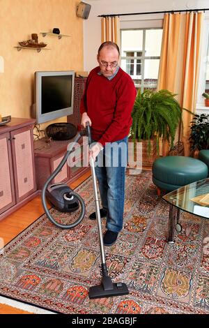 Mann reinigt die Wohnung - Hausarbeit mit einem Staubsauger, MR: Yes Stock Photo
