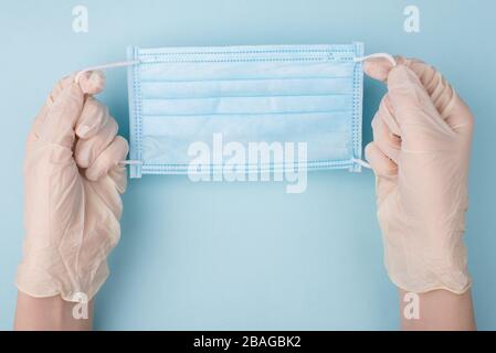 Doctor wearing using medical mask concept. Pov first person view overhead close up view photo of hands holding disposable facial mask isolated over bl Stock Photo