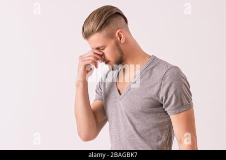 Dissapointed young man touching his head with hand while isolated on white background. Attractove hipster man feeling exhausted or stressed due to har Stock Photo