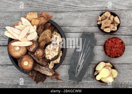 Chinese herbs and acupuncture needles used in traditional herbal medicine on rustic wood background. Stock Photo