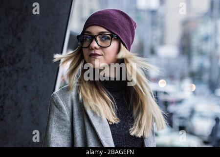 Beautiful stylish hipster woman posing with hair in motion and smiling while standing outdoors. Young girl in eyeglasses and hat turning head around w Stock Photo