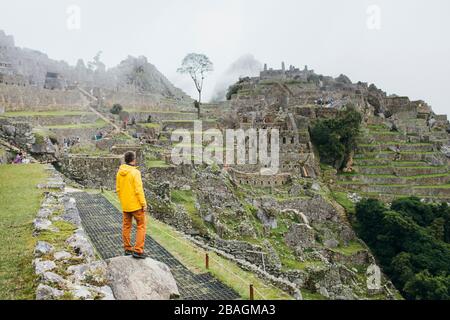 A man in a yellow jacket is standing near ruins of Machu Picchu, Peru Stock Photo