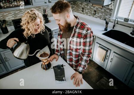 man and woman couple stand together in kitchen making coffee Stock Photo