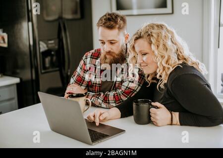 Man and woman couple sit in kitchen with laptop computer and coffee Stock Photo