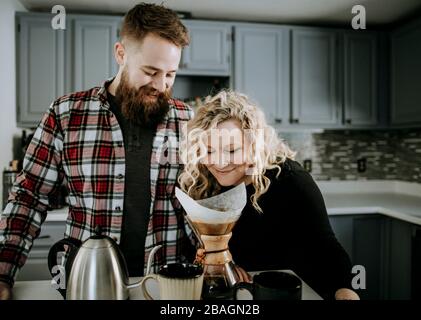 young female smells morning coffee while husband with beard looks on Stock Photo
