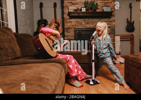 Young girls singing loudly and playing guitar in living room Stock Photo
