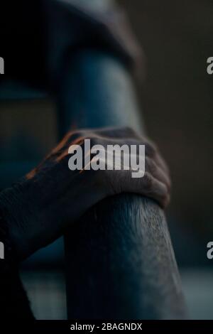 Fragile slim hands of an old lady with Alzheimer's disease, holing on to a wooden rail for balance. Stock Photo