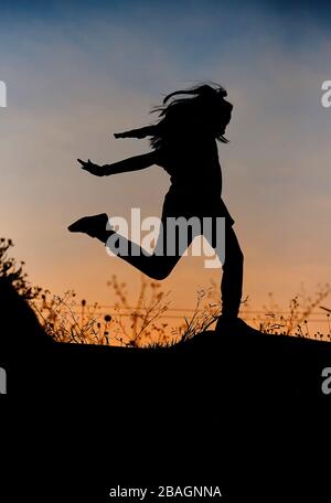 Silhouette of playful girl with sky of sunset Stock Photo