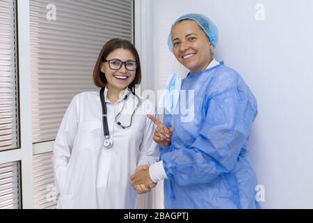 Two positive women colleagues doctors shaking hands and smiling, greeting, congratulations Stock Photo