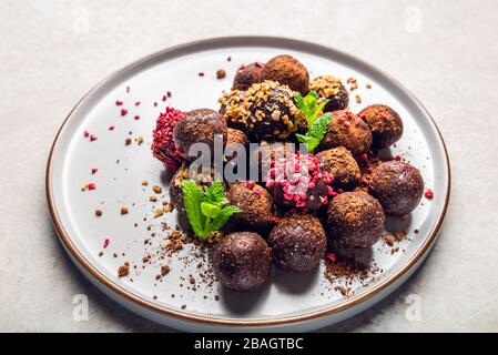 Various Homemade Raw Vegan Truffles or Energy Balls, such as Almond and Cacao, Dark Chocolate and Hazelnut Butter on Grey Plate and Light Background Stock Photo