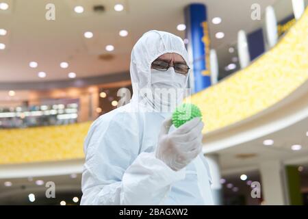 man in coverall disposable anti-epidemic antibacterial isolation suit suspiciously holds in his hand a rubber ball resembling a macro photo of a virus Stock Photo