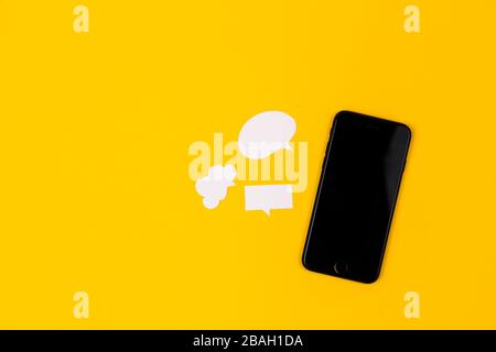 Smartphones with paper speech bubbles on yellow background. Communication concept. Top view. Copy space. Paper composition Stock Photo