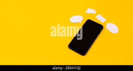 Smartphones with paper speech bubbles on yellow background. Communication concept. Top view. Copy space. Paper composition Stock Photo
