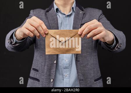 A man in a jacket holding an envelope on a black background. Close up. Stock Photo