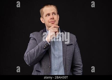 A man in a jacket looking up with a pensive look on a black background. Close up. Stock Photo