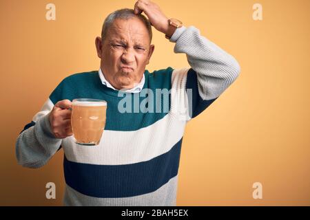 Senior handsome man drinking jar of beer standing over isolated yellow background confuse and wondering about question. Uncertain with doubt, thinking Stock Photo