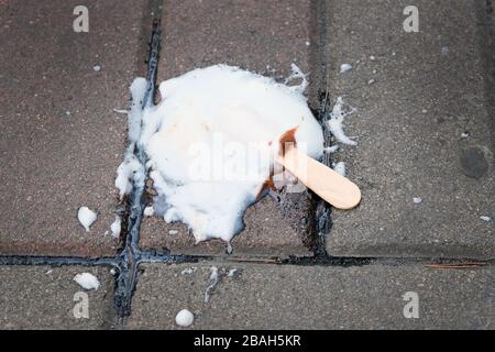 Melted ice cream on a stick on the sidewalk. ice cream bar fell to the floor. ice-cream on a stick white with chocolate. Stock Photo