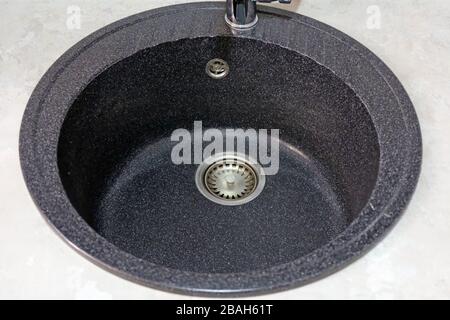 Black round granite sink for the kitchen top view. Granite sink installed in the kitchen countertop and ready for use. Stock Photo