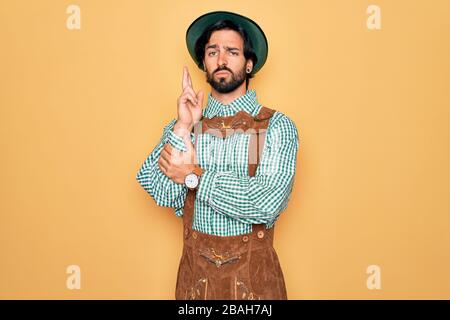 Young handsome man wearing tratidional german octoberfest custome for Germany festival Holding symbolic gun with hand gesture, playing killing shootin Stock Photo