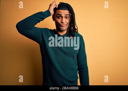 Young handsome african american afro man with dreadlocks wearing green casual sweater confuse and wonder about question. Uncertain with doubt, thinkin Stock Photo