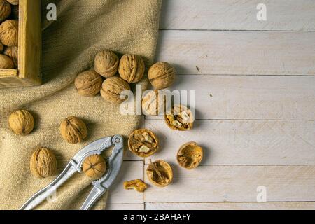 Walnuts in a wooden box, which stands on an old rustic sack, also scattered on a white table nearby is a cracker of walnut Stock Photo