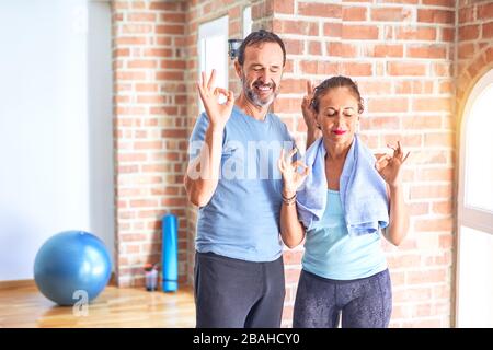Middle age sporty couple standing before do exercise at gym relax and smiling with eyes closed doing meditation gesture with fingers. Yoga concept. Stock Photo
