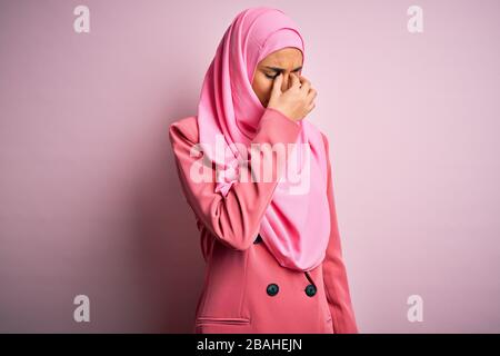 Young beautiful brunette businesswoman wearing pink muslim hijab and business jacket tired rubbing nose and eyes feeling fatigue and headache. Stress Stock Photo