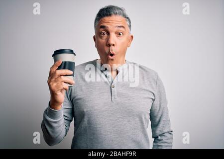 Middle age handsome grey-haired man drinking cup of coffee over isolated white background scared in shock with a surprise face, afraid and excited wit Stock Photo
