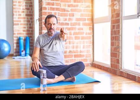 Middle age handsome sportman sitting on mat doing stretching yoga exercise at gym pointing displeased and frustrated to the camera, angry and furious Stock Photo