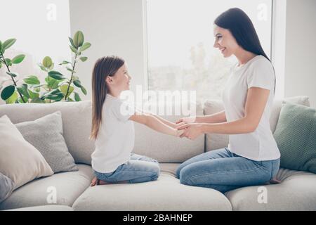 Profile photo of pretty little girl young charming mommy holding arms hands having fun looking eyes sitting comfy sofa spend time weekend together