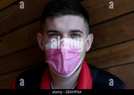 Portrait of smiling young man, wearing medical flu mask on wooden background
