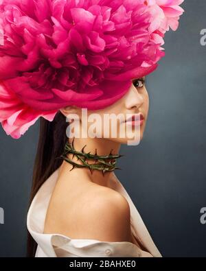 Surreal portrait of a girl with peonies flowers on head and rose thorns on the neck. In Ful Bloom. Interior photo art in art deco style. Beautiful Stock Photo
