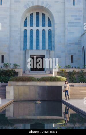 Adding a sense of scale a female tourist stands by the reflection pool in the Hall of memory with the Tomb of the Unknown Soldier in the background. Stock Photo