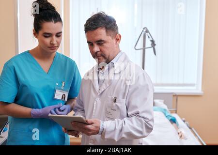 Mature doctor using digital tablet while discussing patients test results with nurse Stock Photo