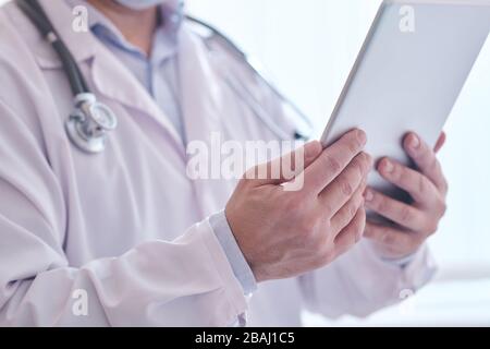 Close-up of unrecognizable doctor in lab coat using digital tablet while analyzing online medical notes Stock Photo