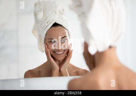 Beautiful woman looking in mirror touches ideal skin feels happy