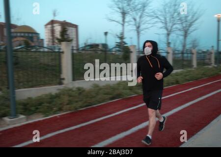 Isolated young man who's wearing mask for protection and a hoodie running at a park Stock Photo
