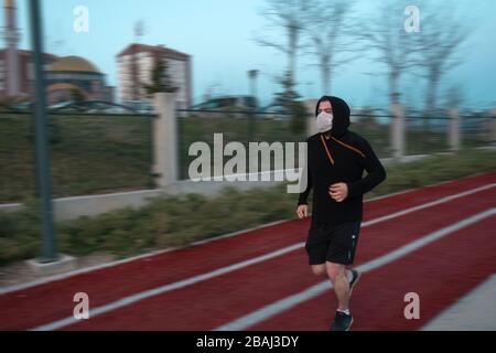 Isolated young man who's wearing mask for protection and a hoodie running at a park Stock Photo