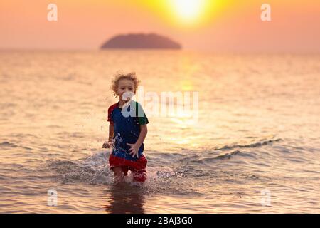 Child playing on ocean beach. Kid jumping in the waves at sunset. Sea vacation for family. Little boy running on exotic island during summer holiday.