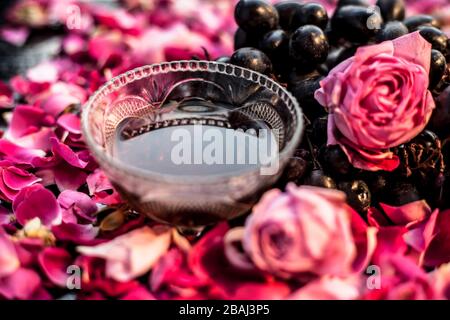 Close up shot of a raw fresh bunch of grapes with some red and pink roses flowers with it on black wooden board. Stock Photo