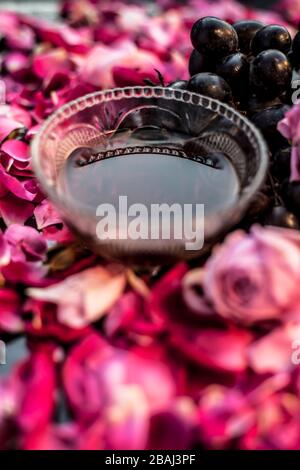 Close up shot of a raw fresh bunch of grapes with some red and pink roses flowers with it on black wooden board. Stock Photo